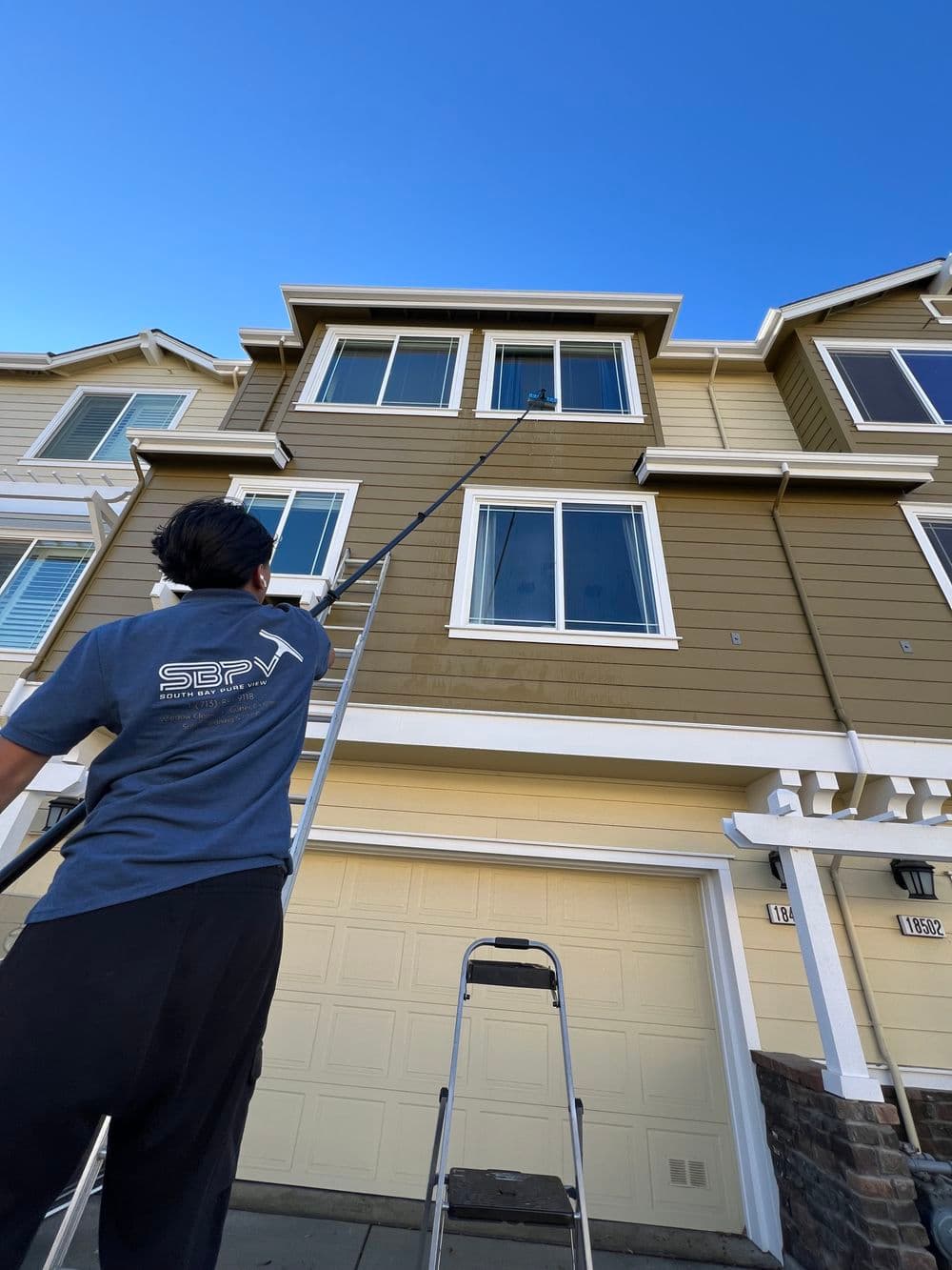 Professional window cleaning service using a pole to reach high windows on a residential building.